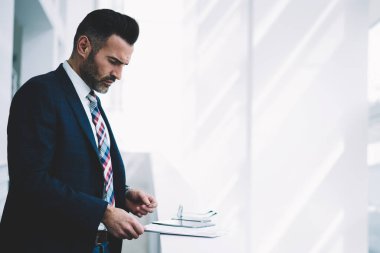 Kendinden emin ve başarılı orta yan görünüm yaşında gurur CEO'su formal giyim ayakta mali şirket ofisinde giyinmiş. Kopyalama alanı alanı yakınındaki belgeleri okuma takım elbiseli ciddi olgun işadamı