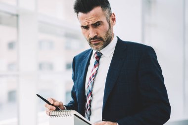 Not Defteri'nde yaparken kameraya bakarak formal giyim giyinmiş emin gurur CEO'su 50 yaşında portresi. Kayıt defter daimi ofis yazma başarılı olgun iş adamı