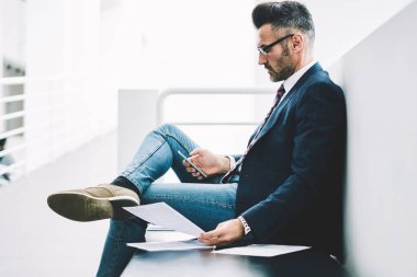 Yan görünüm deneyimli gurur CEO'su orta yaşlı smartphone aygıt üzerinde gelen bildirim bağlı 4 g için okuma Internet. Elinde telefon üstünde posta kontrol belgeleri ile dalgın işadamı