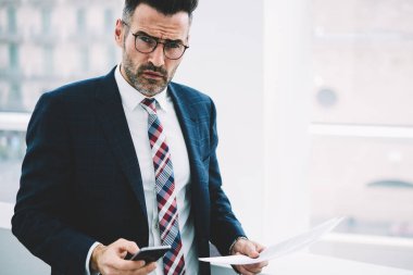 Yarım uzunluk portre emin olgun gurur CEO Smartphone'da kamera arama numarasına süre bakarak takım elbiseli. Hücresel kopya alanı yakınındaki posta kontrol belgeleri ile başarılı ciddi iş adamı