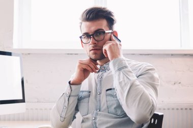 Özgüvenli erkek programcı, arka planda internet reklamınız için boş ekranlı bir evde otururken kameraya bakarak hesap bakiyesini kontrol etmek için operatörle konuşuyor.