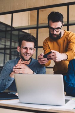 Millennial hipster 'lı gençler birlikte çalışarak bilgisayar ekranının fotoğraflarını çekerken, bilgisayarlı tablet üzerinden SMS mesajları okurken bilgisayarla aynı masada oturuyorlar.