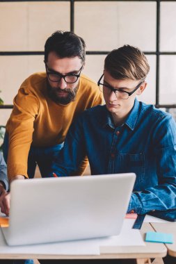 Modern dizüstü bilgisayarda online uygulama üzerinden internetten interneti izleyen bir grup genç erkek iş arkadaşı, yeni başlatılan proje için internet üzerinde araştırma yapan yetenekli adamlar.