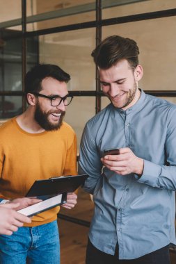 Mutlu erkek arkadaşlar uygulama üzerinden cep telefonuyla sohbet mesajları okuyor, genç adam akıllı telefon cihazında kablosuz interneti kullanarak iş arkadaşlarıyla komik videolar izliyor.