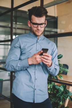 Kafası karışmış Kafkasyalı bir adam akıllı telefon cihazıyla mesaj okuyor. İnterneti tarıyor. Gözlüklü kafası karışık bir hipster modern cep telefonuyla wifi 'ye bağlı online video izliyor.