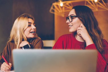 Ödev ödevi sırasında iletişim kuran gülümseyen hipster kızları fikirlerini paylaşıyorlar, kadın en iyi arkadaşlar birlikte çalışma odasında sınav hazırlığı hakkında konuşuyorlar.