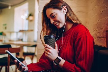 Genç kadın kahve dükkanı, hippi kız dijital tablet üzerinde video çağrısı yapmak için alan coworking içinde wifi kullanarak yeniden oluştururken taşınabilir pc ve elektronik kulaklık online film izlerken