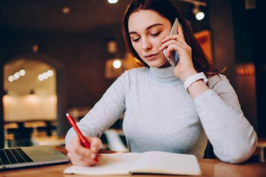 Ciddi kadın serbest meslek distanly kafe, düşünceli erkek danışmanlık için müşteri desteği bankacılık için arama bilgileri belirterek çalışma telefon üzerinde iş görüşme sırasında Notlar yapma