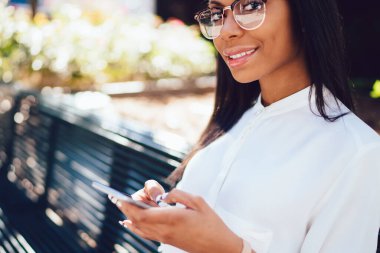 Koyu tenli kameraya smartphone aygıt yolu ile şehir merkezindeki bankta oturmuş 4 g internet bağlantısı üzerinde online sohbet mesajlaşma süre gülümseyen başarılı çekici genç kadın portresi kırpılmış