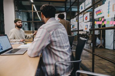 Gündelik giysiler içinde bir grup çok ırklı iş arkadaşı masamızda dizüstü bilgisayarla oturmuş modern ofiste çalışırken projenin detaylarını tartışıyorlar.