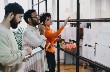 Günlük giysiler içinde bir grup genç iş arkadaşı tablet kullanırken beyin fırtınası sırasında ayrıntıları tartışıyor ve gelecekteki projeler hakkında konuşuyorlar.