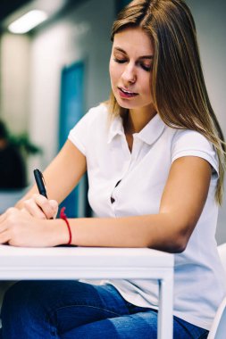 Dalgın kız öğrencinin Üniversite Kütüphane bilgi ve fikir notları ders planlama yazma not defterinde yapma akıllı hippi kız ile dizüstü bilgisayar, masada oturan taşkın ödev