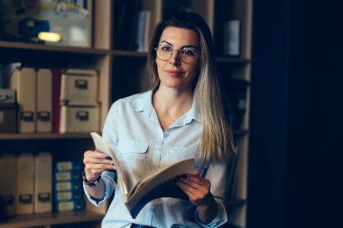 Genç büyüleyici pozitif düşünceli kadın kişi uzakta Kitaplığı'nda otururken seyir daha iyi görüş için gözlük. Boş vakit ellerini dergide holding muhteşem hippi kız