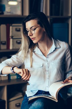 Genç çekici dalgın kız öğrenci Kitaplığı'nda Toplantı için beklenirken kol saati zamanında kontrol şık gömlek giymiş. Şirin ciddi kadın kapalı oturma sırasında çalışma programı planlama