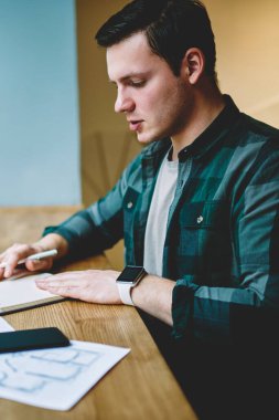 Genç adam akıllı erkek öğrenci ile kağıt ve Kırtasiye kafede oturan üniversite sınavları için hazırlık kurs projesinin planlama iç yapım coworking uzayda öğrenme konsantre