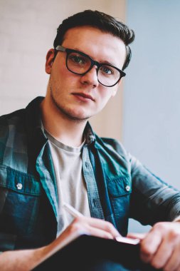 Gözlük vizyon düzeltme mesafe iş sürecinde, profesyonel erkek serbest kamera Cafe bakarak yayın makaleleri notlar yapmak için ciddi hipster adam portresi