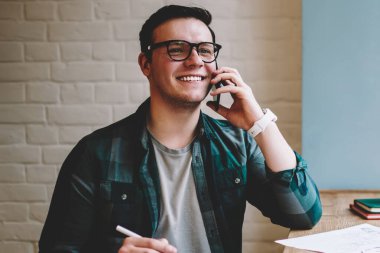 Neşeli erkek serbest meslek sahibi iyi ruh hali planlayıcısı yazma eğitimi sırasında smartphone konuşmayı kafe iç, mutlu hipster adam çalışan proje hakkında telefon paylaşım iyi haber verme