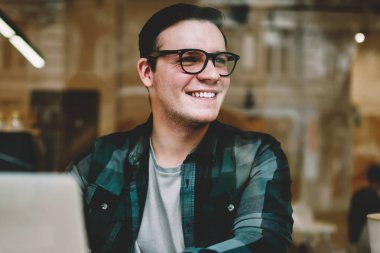 Neşeli hipster erkekte erkek öğrenci uzak yazarak geribildirim online sohbet arıyorsunuz gözlük gülümseyen serbest dizüstü bilgisayar, café iç yazarak yayın makale zevk gözlükler