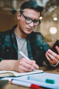 Telefon, cep telefonu teknolojisi ile office coworking oturan kişiden belirterek konsantre adam freelancer tutan Not defterinizdeki bilgileri yazma Eyewear düşünceli erkek öğrenci