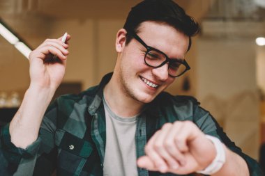 Hippi erkek erkeğe yönetme zaman giyilebilir bilgisayar ekran kafede bakarak Ajanda'yı kullanarak gülümseyen yararlı uygulamalar dijital smartwatch dokunmatik ekran, seyir üzerinde neşeli erkek öğrenci memnun