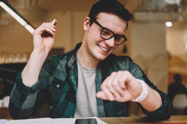 Hippi erkek erkeğe yönetme zaman giyilebilir bilgisayar ekran kafede bakarak Ajanda'yı kullanarak gülümseyen yararlı uygulamalar dijital smartwatch dokunmatik ekran, seyir üzerinde neşeli erkek öğrenci memnun