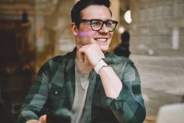 Neşeli hipster adam uzakta smartphone, müreffeh erkek freelancer mesafesi iş modern aygıtlar ve kablosuz internet ile kafeterya iç memnun tutan penceresinde arıyorum gözlükler