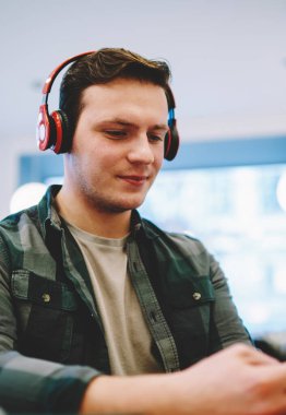 Hipster adam kırmızı kulaklık alan, genç erkek telefonda app üzerinden görüntülü görüşme yapmak için bluetooth kulaklık kullanarak coworking içinde serbest zaman sırasında Smartphone cep telefonu ile en sevdiğiniz film online izlemek