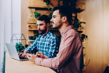 Genç erkek meslektaşları dizüstü bilgisayar, netbook kampüsünde oturan araştırma yapma üniversite proje üzerinde iki hipsters çocuklar takım kullanarak alan coworking içinde serbest uzaktan birlikte çalışma