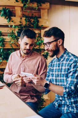 Gülümseyen hippi çocuklar dijital tablet ve modern uygulamalar kullanarak boş zamanlarını geçiriyorlar, sakallı erkek dokunmatik dokunmatik oyunlar oynuyor ve arkadaşlarıyla kampüste boş zamanlarında konuşuyorlar.