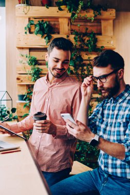 Konsantre hipster adam telefonda gelir mesajı okurken arkadaşı ilginç, yetenekli iş arkadaşları modern teknolojiyi kullanarak iş birliği yapmayı planlıyorlar.