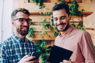 Neşeli hipster çocuklar birlikte gülüyor pay yolu ile bluetooth bağlantı, komik ortak fotoğraf kaygısız erkek öğrencilerin sosyal ağlar güncelleştirmelerini denetlemek için dijital cihazlar kullanarak birbirleri ile şaka