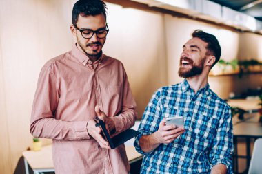 Genç gülümseyen hipster adam meslektaşım tarafından tatilinde ofiste, arkadaş onun komik resimler e-posta alma Smartphone'da ağ üzerinde şaka duygusal neşeli adam komik hikaye gülüyorsun