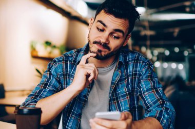 Düşünceli bir erkek, internet sitesinde yer ayırtma hakkında bilgi toplarken, kafası karışmış hipster adam, akıllı telefondan e-posta kontrol makbuzu almak için kafa yoruyor.