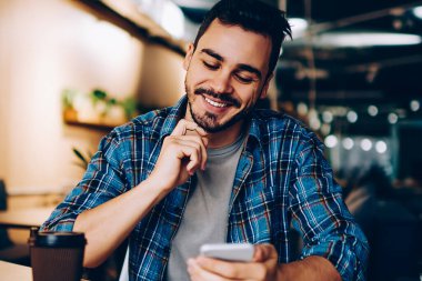 Sosyal ağlarda yeni mesajlar okuyan gülümseyen yenilikçi adam akıllı telefondan yeni bir arkadaşı doğruladı, cep telefonu bakiyesindeki bankacılık uygulamasından memnun olan genç adam öğrenirken cep telefonu bakiyesini kontrol ediyor.