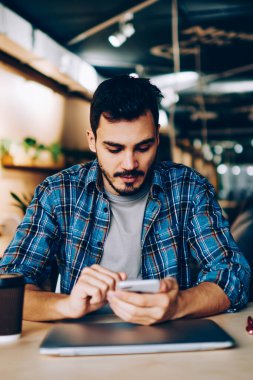 Bildirim gelir çıkıyor öğrenme için üniversite kafeteryada otururken hücresel, genç erkek yükleme uygulaması üzerinde cep telefonu sosyal ağlardan kontrol dalgın hipster adam