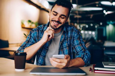 Sosyal ağlarda yeni mesajlar okuyan gülümseyen yenilikçi adam akıllı telefondan yeni bir arkadaşı doğruladı, cep telefonu bakiyesindeki bankacılık uygulamasından memnun olan genç adam öğrenirken cep telefonu bakiyesini kontrol ediyor.