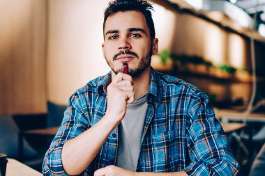 Kameraya bakan düşünceli hipster adam kütüphanede dizüstü bilgisayarla ödev yapmaya odaklanmış yaratıcı erkek yazar ağ profilinde yayınlanması için makale yazmayı düşünüyor.