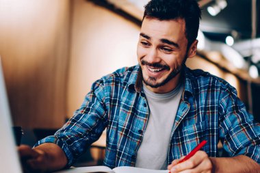 Ödev hazırlama kitaplığı, mutlu erkek öğrenci öğrenme sırasında netbook komik video izleme sırasında dizüstü bilgisayarda sosyal ağlar içeriğine bakın gülüyor neşeli hipster adam göz