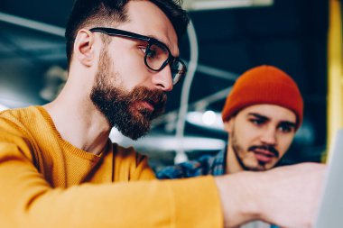 Yetenekli erkek, geliştirme eğitmeni, dizüstü bilgisayarı işaret eden eğitmen ve arkadaşlarıyla iletişim kuran hipster bir adamın internet sitesinde yeni bir uygulama göstermesi.