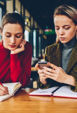 Yetenekli öğrenci test kadın öğretmen Smartphone cep telefonu ile bildirim coworking özel ders sırasında okuma sırasında Not Defteri'nde aşağı yazma. İki hippi kız cep üzerinde internet kullanımı semineri için hazırlanıyor
