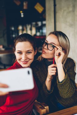 Casual giyim poz ve selfie fotoğraflar yayın için modern smartphone cep telefonu ile sosyal ağlar kafede dostu toplantı sırasında iç yapım komik suratlar ile iki başarılı kadın blogcular