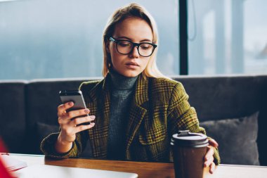 Ciddi kadın blogger giyinmiş elinde masada oturan ve e-posta için 4 g bağlı smartphone aygıt üzerinde kontrol gitmek için kahve alarak zarif ceketli Internet. Hücresel kafede dinlenme ile öğrenci