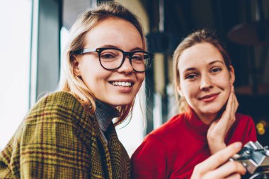 Mutlu yetenekli kadın Amatör kamera şık kahve dükkanında dinlenme olumlu en iyi arkadaşı ile birlikte gülüp, yarı uzunluk portre. Neşeli iki öğrenci ile coworking içinde oturan vintage fotoğraf makinesi
