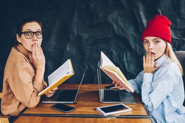 Kameraya alan coworking içinde sınava hazırlık sırasında şaşkın yüzler ile arıyorum elinde kitap okuyan ile heyecanlı iki hipster öğrenci portresi. Şok gençler bilgi öğrenme