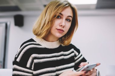 Yarım uzunluk portre sarışın profesyonel tasarımcı akıllı bilgi aramak için 4 g bağlıyken kameraya bakarak kısa saç kesimi ile dizüstü bilgisayar ofiste oturan internet