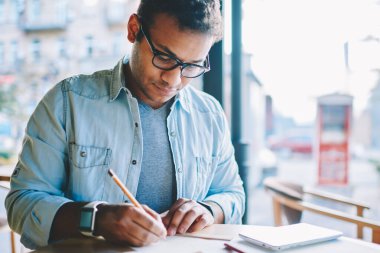 Kırpılmış görüntü yakışıklı zeki erkek mimar skeçler kalem ve cetvel kullanarak kağıt üzerine çizim şık kot elbise giymiş. Bazı bilgiler kapalı ölçme akıllı hipster adam durulması