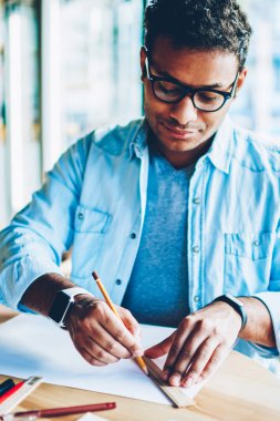 Durulması akıllı yetenekli erkek mimar planları yeni ofis binası için çizim rahat kıyafetler giymiş. Kalem ve kural kullanarak kafeteryada çalışan Eyewear düşünceli akıllı hindu çalışan