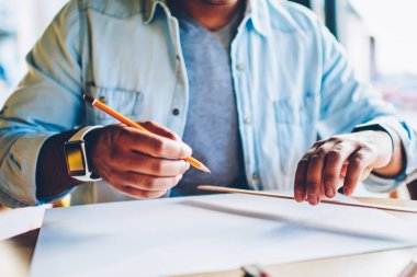 Kırpılmış görüntü akıllı yaratıcı erkek mimar planları üzerinde kapalı oturma sırasında çalışma trendy kot elbise giymiş. Kalem ve kural skeçler oluşturulurken holding adam eller odaklanmak