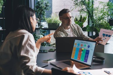 Erkek ve kadın meslektaşlar, iş birliği sırasında bilgisayarlarla iş pazarlamasını tartışan, beyin fırtınası sırasında bilgi grafikleriyle belgeleri analiz ediyorlar.