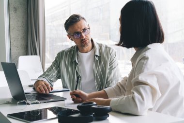 Optik gözlük takan erkek çalışanlar, masaüstü bilgisayarındaki işbirliği sırasında kadın meslektaşlarıyla iletişim kuruyor. Profesyonel girişimciler konuşuyor.